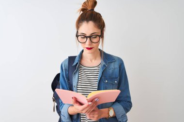 Redhead öğrenci kadın ciddi düşünme akıllı yüz üzerinde emin bir ifade ile izole beyaz arka plan üzerinde sırt çantası okuma kitabı giyiyor