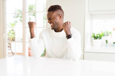 Beyaz masada yakışıklı Afrikalı Amerikalı adam çok mutlu ve heyecanlı silah ile kazanan jest yaparak, gülümseyen ve başarı için çığlık kaldırdı. Kutlama konsepti.