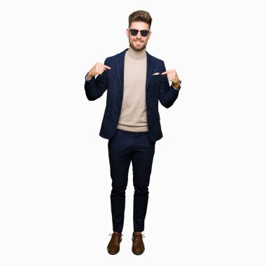 Genç yakışıklı zarif adam yüzünde gülümseme ile kendinden emin görünüyorsun, kendini gururlu ve mutlu parmakları ile işaret güneş gözlüğü takıyor.