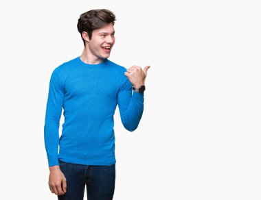 Yakışıklı delikanlı arıyor ve başparmak yanında yukarıyı mutlu yüz ile gülümseyen izole arka plan üzerinde mavi kazak giyiyor.
