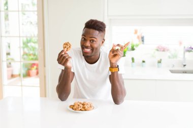 Genç Afro-Amerikan adam yeme çikolata Çerezler el ve parmak ile tarafına işaret çok mutlu fişleri