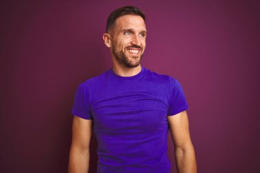 Lila izole arka plan üzerinde rahat mor t-shirt giyen genç adam yüzünde gülümseme, doğal ifade ile yan bakıyor. Gülmekten emin.