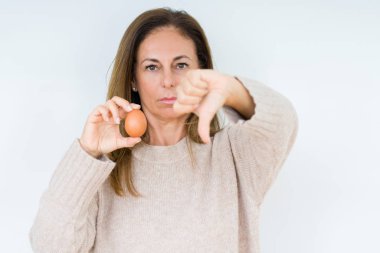 Kızgın yüz, eksi işareti aşağı antipati başparmak ile gösterilen, ret kavramı ile izole arka plan üzerinde taze yumurta tutan orta yaş kadın