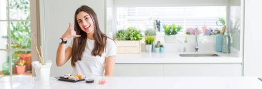 Teslimattan asya suşi yiyen güzel genç kadının geniş açılı resmi telefonda konuşmak gibi el ve parmaklarla telefon hareketi yaparak gülümsüyor. İletişim kavramları.