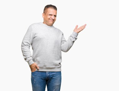 Neşeli sunulması ve kameraya bakarak avucunun ile işaret gülümseyen izole arka plan üzerinde spor kazak giyen orta yaş Arap adam.