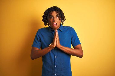 Yalnız sarı arka plan üzerinde duran rahat kot gömlek giyen dreadlocks ile Afro adam yalvarıyor ve çok duygusal ve endişeli yüzünde umut ifadesi ile birlikte elleri ile dua. Af dilemek istiyorum. Din kavramı.