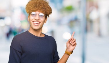 Gözlüklü kocaman bir gülümseme ile yüzünde, afro kameraya bakarak yan el ve parmak ile işaret eden genç yakışıklı adamla.