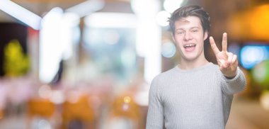 Gösterilen arka plan üzerinde kış kazak giyen genç yakışıklı adam izole ve parmakları ile işaret kendinden emin ve mutlu gülümseyerek ise ikinci.