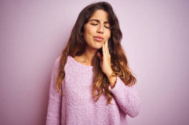 Genç güzel kadın pembe izole arka plan üzerinde duran kazak giyen diş ağrısı veya diş üzerinde diş hastalığı nedeniyle ağrılı ifade ile el ile ağız dokunmadan. Diş hekimi konsepti.