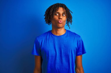 Dudaklar, çılgın ve komik jest ile balık yüz yapma izole mavi arka plan üzerinde duran t-shirt giyen dreadlocks ile Afro Amerikan adam. Komik ifade.