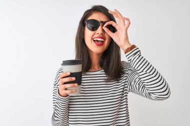 Güneş gözlüğü içen Çinli kadın parmakları ile bakarak göz üzerinde el ile ok işareti yapıyor gülümseyerek mutlu yüzü ile izole beyaz arka plan üzerinde kahve götürmek