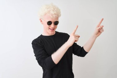 Genç albino adam siyah t-shirt giyen ve sunglasess izole beyaz arka plan üzerinde gülümseyerek ayakta ve yan iki el ve parmak ile işaret kamera bakıyor.