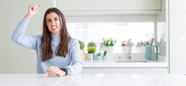 Evde beyaz masada oturan güzel genç kadının geniş açılı resmi kızgın ve öfkeli yükselterek yumruk sinirli ve öfkeli öfke ile bağırırken. Öfke ve agresif kavram.