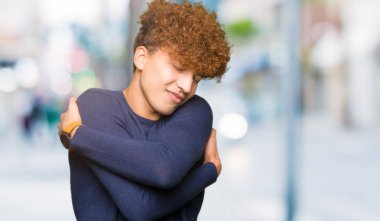 Kendini mutlu ve olumlu sarılma, kendinden emin gülümseyen afro saçlı Genç yakışıklı adam. Kendi aşk ve öz bakım
