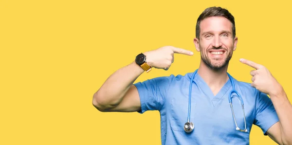 英俊的医生在孤立的背景穿着医疗制服微笑自信显示和指向用手指的牙齿和嘴 健康理念 — 图库照片