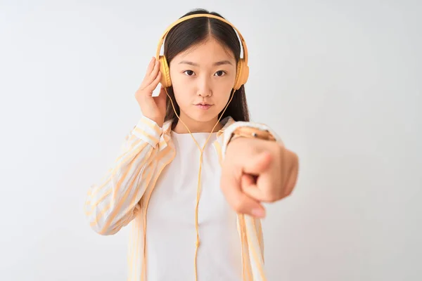 Young chinese woman listening to music using headphones over isolated white background pointing with finger to the camera and to you, hand sign, positive and confident gesture from the front