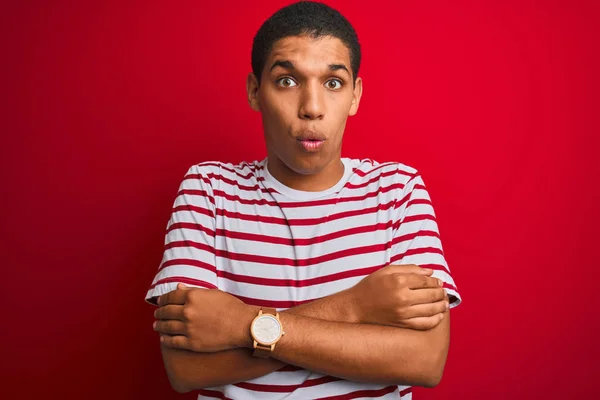 Young handsome arab man wearing striped t-shirt over isolated red background shaking and freezing for winter cold with sad and shock expression on face