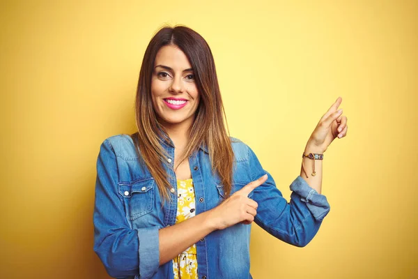 Young beautiful woman standing over yellow isolated background smiling and looking at the camera pointing with two hands and fingers to the side.