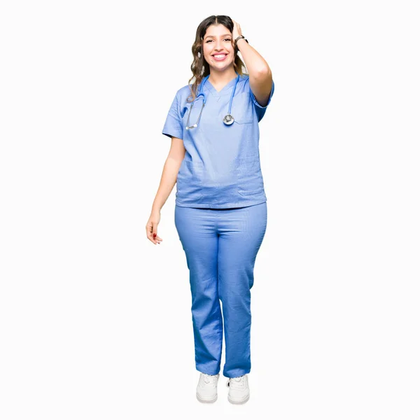 医療制服の笑顔 ジェスチャーを手で髪に触れる自信を持って魅力的なポーズを身に着けている若い大人医師女性 — ストック写真