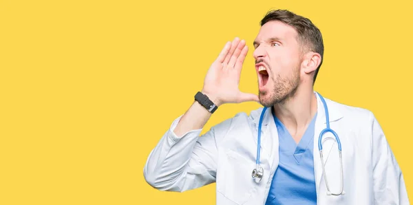 帅气的医生在孤立的背景下穿着医疗制服 大声喊话 用手放在嘴边尖叫 沟通理念 — 图库照片