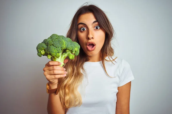 Young beautiful woman eating broccoli over grey isolated background scared in shock with a surprise face, afraid and excited with fear expression