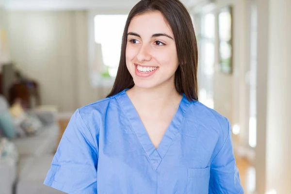 Beautiful young nurse woman at the clinic looking away to side with smile on face, natural expression. Laughing confident.