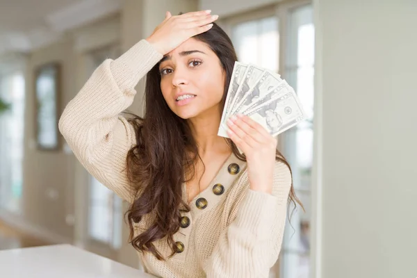 Young woman holding 20 dollars bank notes stressed with hand on head, shocked with shame and surprise face, angry and frustrated. Fear and upset for mistake.