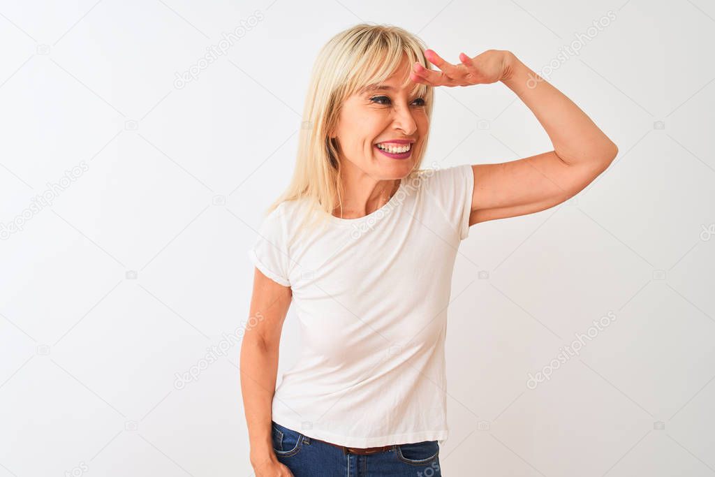 Middle age woman wearing casual t-shirt standing over isolated white background very happy and smiling looking far away with hand over head. Searching concept.