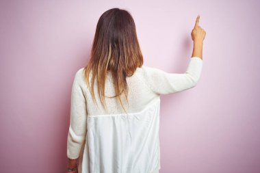 Genç güzel kadın pembe izole arka plan üzerinde duran parmak el ile ileriye işaret geriye doğru poz