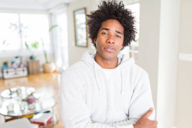 Kazak giyen Afro-Amerikan adam yüzünde ciddi bir ifade ile rahat. Çapraz kollarla basit ve doğal