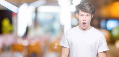 Casual beyaz giyen genç yakışıklı adam şüpheci ve alaycı, t-shirt üzerine şok karşısında izole arka plan açık ağız ile şaşırttı.