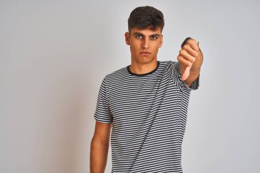 İzole beyaz arka plan üzerinde duran lacivert çizgili t-shirt giyen genç hintli adam mutsuz ve kızgın gösteren reddi gösteren ve başparmak aşağı jest ile negatif. Kötü ifade.
