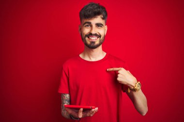 Kendine parmak işaret sürpriz yüzü ile izole kırmızı arka plan üzerinde duran tablet kullanarak dövme ile genç adam