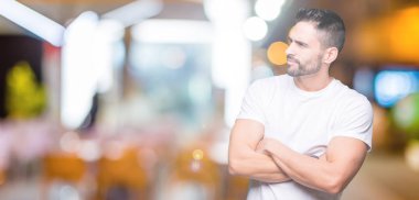 Yakışıklı adam gece açık havada arka plan üzerinde beyaz t-shirt giyen kollarını ile yan bakarak gülümseyerek ikna ve kendinden emin geçti