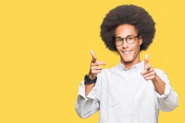 Afrikalı-Amerikalı genç afro saçlı gözlüklü fotoğraf makinesi ile mutlu ve komik yüz için parmakları işaret. İyi enerji ve vibes.