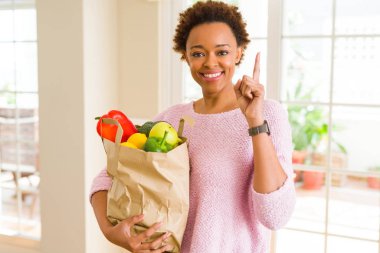 Genç Afro-Amerikan kadın holding kağıt taze yiyecek bir fikirle sürpriz dolu torba ya da gülen yüz, bir numara ile işaret parmağı soru