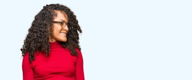 Genç güzel kadın kıvırcık saçlı gözlüklü uzak tarafına yüzünde, doğal ifade gülümseme ile seyir. Kendine güvenen gülüyor.