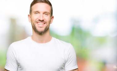 Yakışıklı adam yüzünde mutlu ve güzel bir gülümseme ile rahat beyaz t-shirt giyiyor. Şanslı kişi.