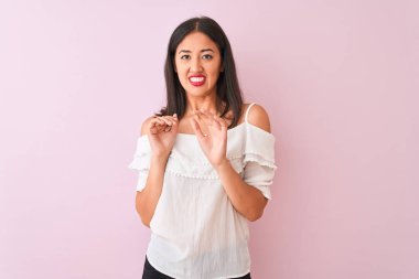İzole edilmiş pembe arka plan üzerinde duran beyaz tişört giyen güzel Çinli kadın iğrenmiş ifade, hoşnutsuz ve korkulu tiksinti yüz yapıyor çünkü nefret tepki. Elleri havada. Sinir bozucu kavram.