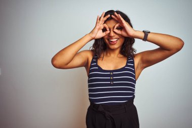 Eforel transseksüel kadın izole beyaz arka plan üzerinde çizgili t-shirt giyen dürbün dil dışarı yapışmasını gibi ok jest yapıyor, gözleri parmaklardan bakarak. Çılgın ifade.