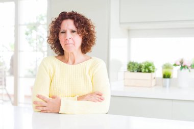 Sarı kazak giyen güzel yaşlı kadın şüpheci ve sinirli, çapraz kolları ile yüzünde onaylamayan ifade. Negatif kişi.