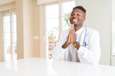 African american doctor man at the clinic praying with hands together asking for forgiveness smiling confident. clipart