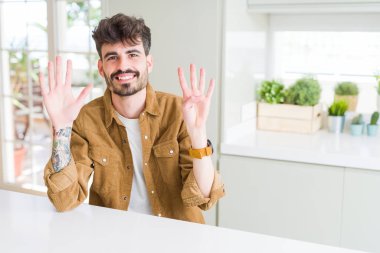 Beyaz masanın üzerinde oturan rahat ceket giyen genç adam, kendinden emin ve mutlu gülümserken parmaklarıyla dokuz numarayı göstererek ve işaret ediyor..