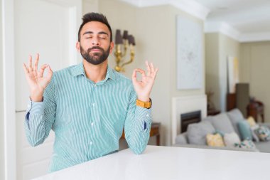 Yakışıklı adam evde sakin ol İspanyol ve gülümseyen gözlerle parmak ile meditasyon jest yapıyor kapalı. Yoga kavramı.
