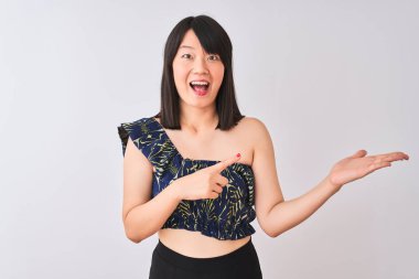 Genç güzel Çinli kadın izole beyaz arka plan üzerinde yaz çiçek t-shirt giyen hayran ve el ile sunarken kameraya gülümseyerek ve parmak ile işaret.