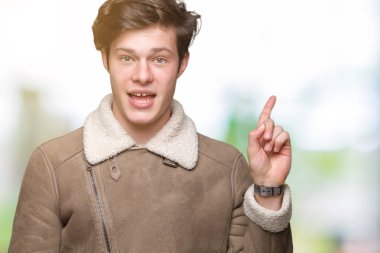 Yüz üzerinde büyük bir gülümseme ile izole arka plan üzerinde kış ceket giyen genç yakışıklı adam, kamera bakarak yan el ve parmak ile işaret.