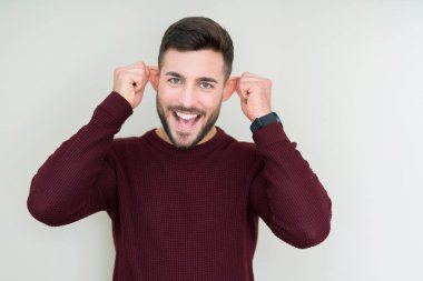 Genç yakışıklı adam izole arka plan üzerinde bir kazak giyen gülümseyerek parmakları ile kulakları çekerek, komik jest. Seçme sorunu