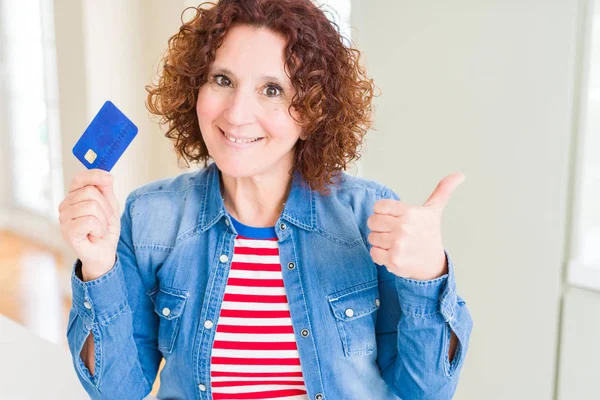 Senior woman holding credit card as payment pointing and showing with thumb up to the side with happy face smiling