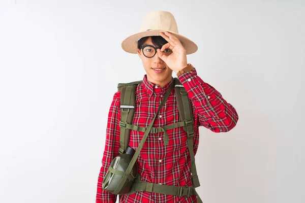 Chinese hiker man wearing backpack canteen glasses hat over isolated white background doing ok gesture with hand smiling, eye looking through fingers with happy face.