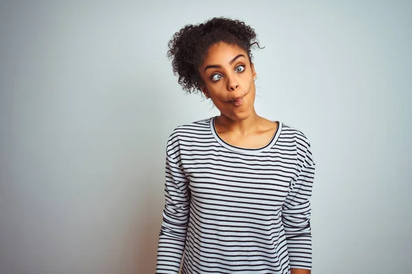 African american woman wearing navy striped t-shirt standing over isolated white background making fish face with lips, crazy and comical gesture. Funny expression.
